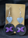 Silver hearts atop black circles with back facing people and silver moons