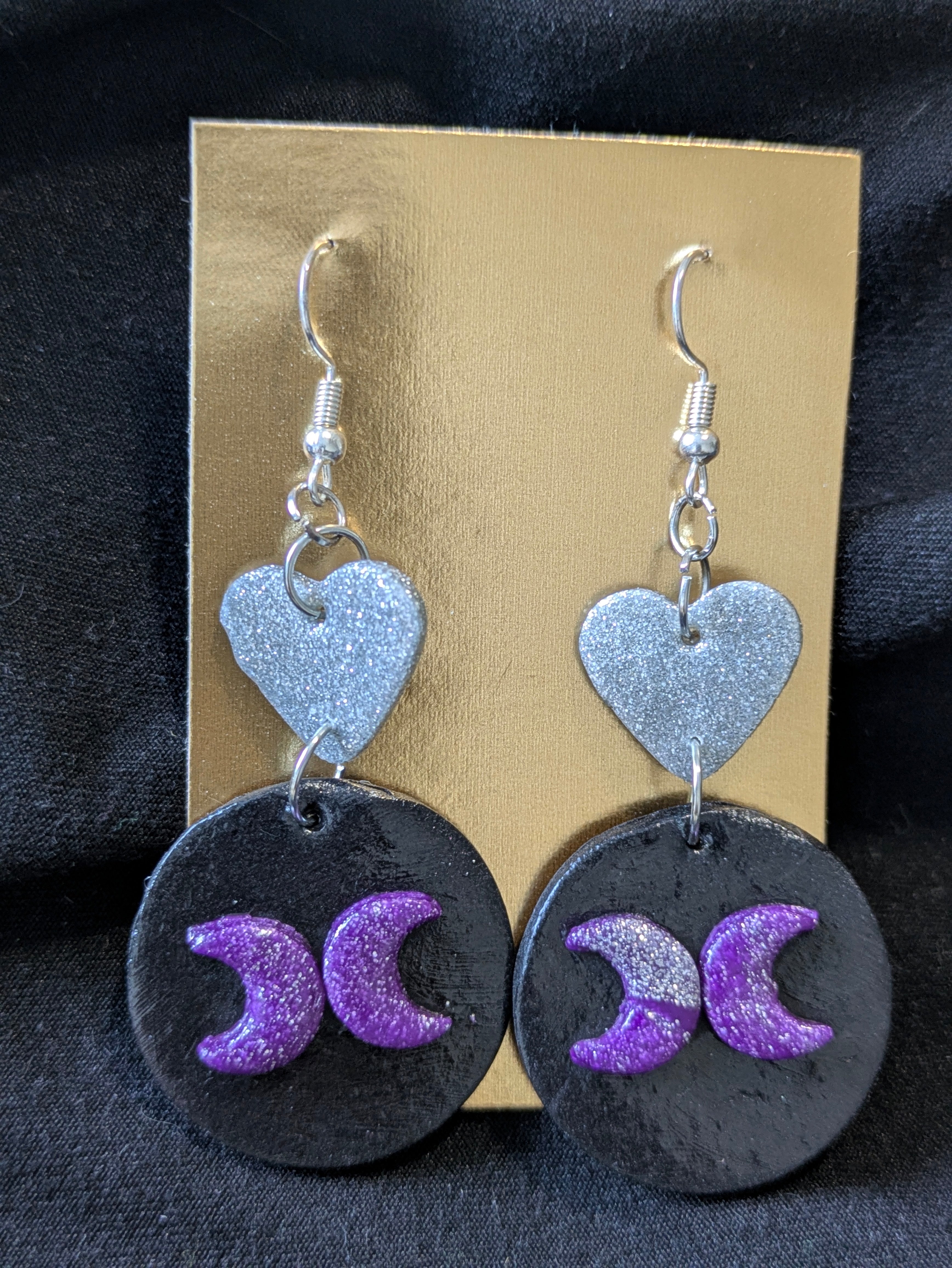 Silver hearts atop black circles with back facing people and silver moons